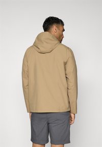 Beige hettejakke med en glatt tekstur, som har bakstykke og elastiske mansjetter, kombinert med grå shorts. Enkel design uten dekorasjoner.