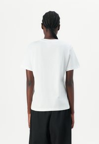 Camiseta de algodón blanca con un corte relajado y mangas cortas, que presenta un sencillo cuello redondo y sin logotipos ni patrones visibles.