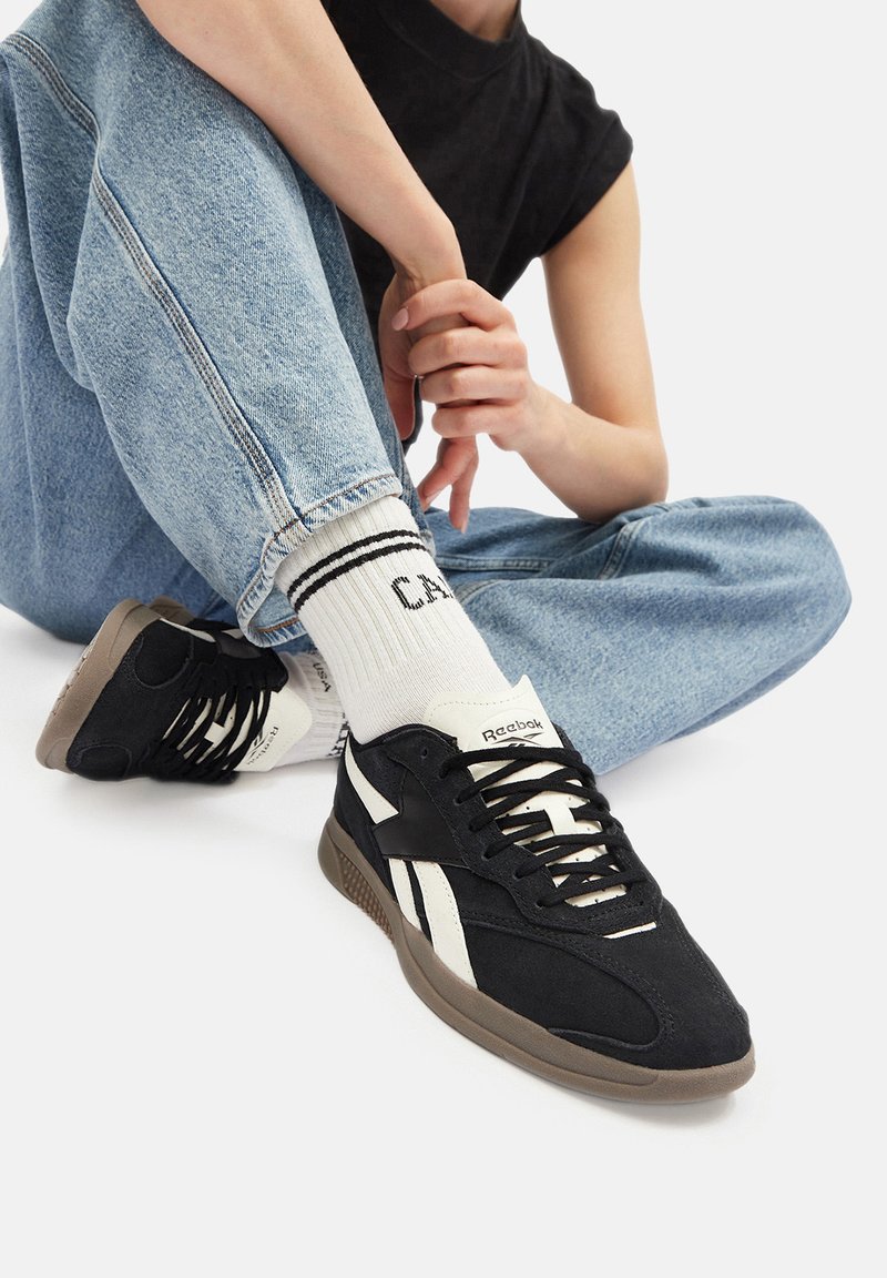 Mustvalged ja valged spordijalatsid tekstuuriga ülemise osaga, millel on paelad, kummist talla ja logo keeles, koos siniste teksade ja triibuliste sokkidega.