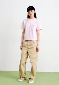 Rosa bomullströja med bröstficka, i kombination med beigefärgade vidbyxor. Svartkeps med vit text och beiga sneakers fulländar stilen.