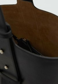 Bolso tote de cuero negro con un interior de ante marrón, que cuenta con un bolsillo con cremallera y texturas suaves, destacando elementos de diseño prácticos.