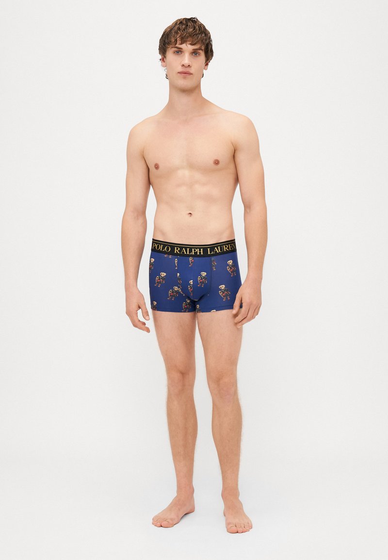 Bañadores ajustados en azul marino con un patrón decorativo de esqueletos, con una cinturilla negra que lleva la inscripción "POLO RALPH LAUREN" en letras doradas.