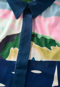 Chemise à boutons avec un motif abstrait coloré. Fabriquée en tissu lisse, avec un col et une patte de boutonnage sombres aux teintes pastel.