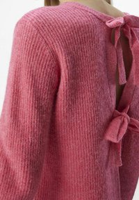 Pull rose en tricot avec une surface texturée, présentant une découpe profonde dans le dos et deux nœuds noués en haut, créant un design dos nu.