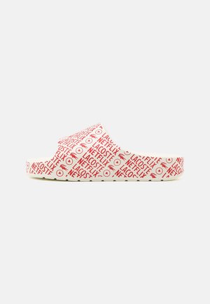 Slip-on schoen met witte basis bedekt met rode herhalende Lacoste en Netflix logo's en symbolen, zijaanzicht tegen een effen achtergrond.