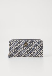 Beige wallet with navy geometric pattern and gold logo hardware. Zipper closure and contrasting dark trim. Smooth fabric texture.