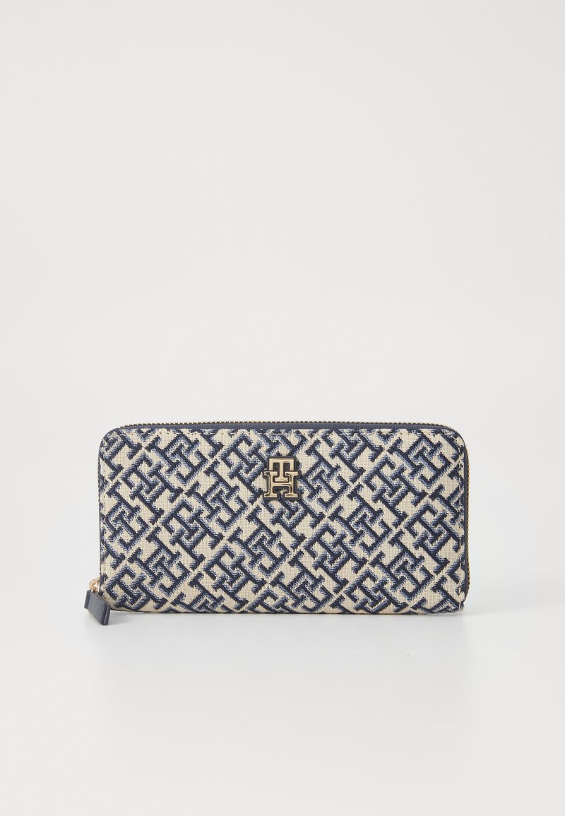 Portafoglio beige con motivo geometrico navy e hardware logo dorato. Chiusura con zip e bordo scuro a contrasto. Tessuto dalla texture liscia.