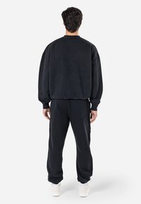Sudadera negra y pantalones a juego de tejido suave. Corte relajado con puños y cintura acanalados. Cuenta con un cuello redondo y un diseño minimalista.