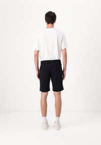 Black shorts with a tailored design, feature side and back pockets, paired with a plain white t-shirt and light-colored sneakers.