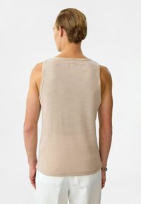 Beige, aansluitend zonder mouwen tanktop gemaakt van een zachte, geribbelde stof. De achterkant heeft een eenvoudig ontwerp zonder versieringen.