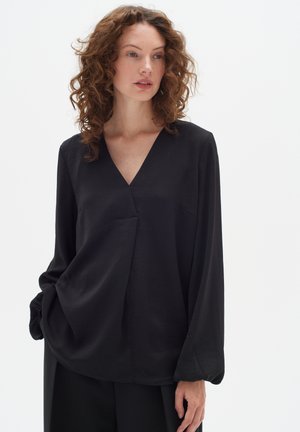Black long-sleeve top in soft fabric, featuring a deep V-neck and a loose fit with a slight drape and side pockets.