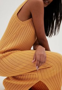 Robe tricotée jaune moutarde à rayures verticales, design sans manches avec une fente latérale, dotée d'une finition texturée et d'une coupe décontractée.