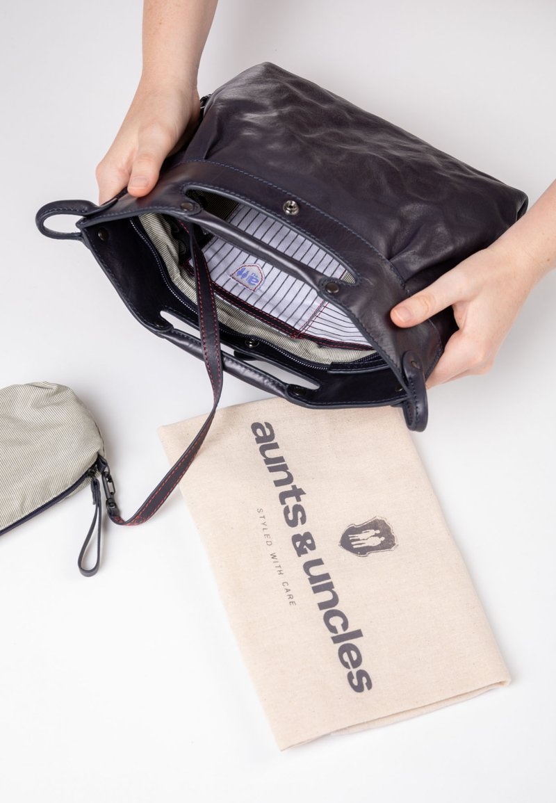 Dunkelblaue Lederhandtasche mit zwei Griffen, gestreiftem Stoffinneren und roten Nähakzenten. Inklusive leichtem Leinenschutzbeutel.