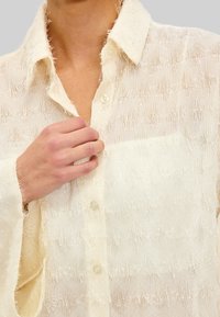 Witte doorschijnende blouse met knopen, versierd met gestructureerde franjes, voorzien van een spreidkraag en een borstzak. Zachte stof en losse pasvorm.