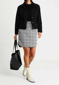 Veste en denim noire sur un top noir, avec une jupe à carreaux grise. Un sac fourre-tout noir et des bottines blanches à talons complètent la tenue.