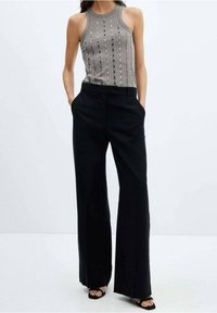 Grijs gebreid tanktop met verticale ribbels, gecombineerd met zwarte broek met brede pijpen. De outfit heeft zakdetails en wordt gedragen met zwarte sandalen.