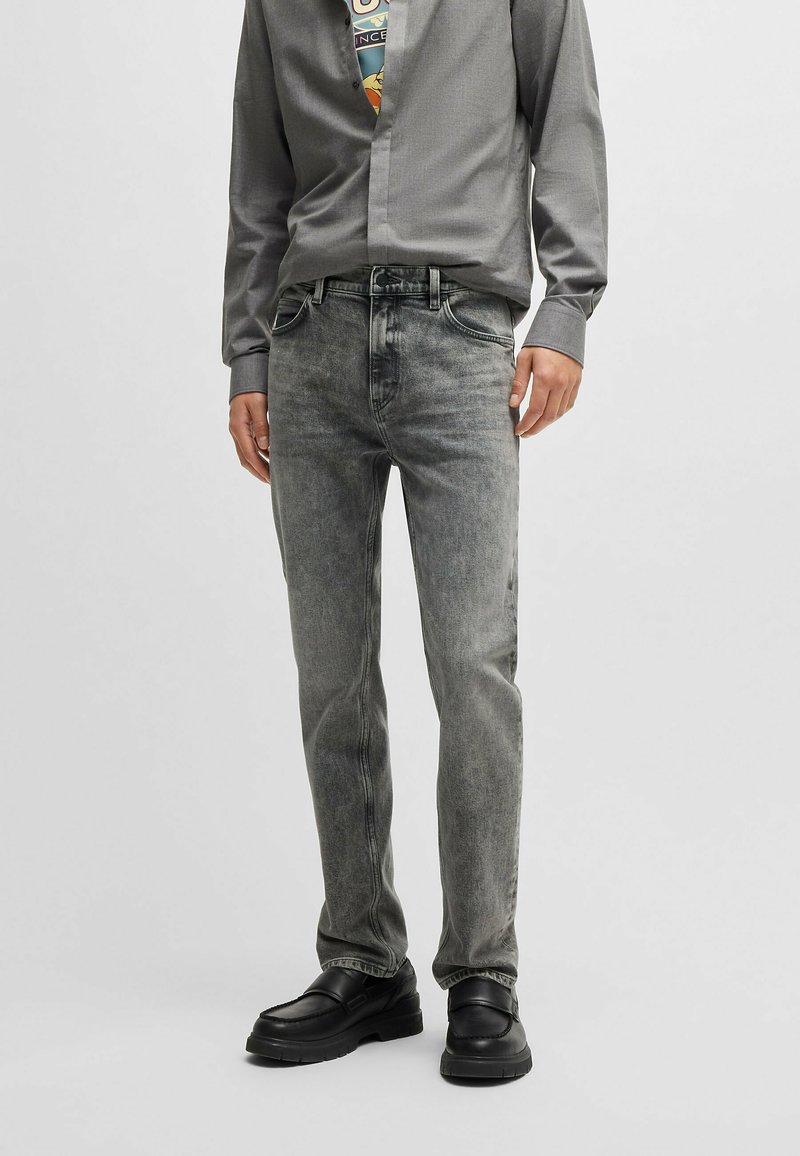 Jeans in denim grigio con una vestibilità slim, caratterizzati da una finitura sbiadita, cinque tasche e gamba dritta. Abbinati a una camicia con bottoni.