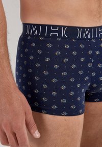 Navy boxer briefs with a fitted design, made of soft fabric. Features a geometric pattern in light blue, yellow, and white. Branding on waistband.