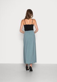 Zwarte top met dunne bandjes, gecombineerd met een lange, flowy, mintgroene rok. Model draagt zwarte hoge hakken. Eenvoudig ontwerp.