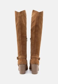 Καφέ σουέτ μπότες μέχρι το γόνατο με σχήμα λαιμού, με πλευρικούς φερμουάρ και ανθεκτικό τακούνι τύπου μπλοκ. Διαθέτουν μια διακοσμητική λωρίδα κοντά στον αστράγαλο.