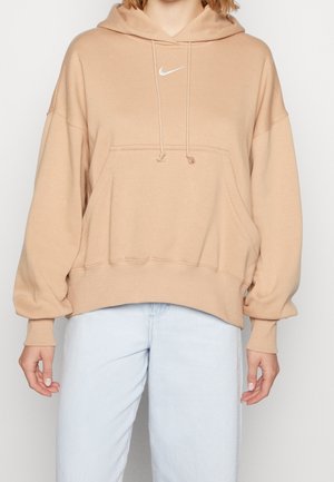 Sweat à capuche beige Nike avec poche frontale et cordons, porté avec un jean bleu clair, visible des épaules aux hanches.