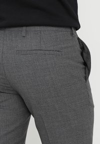Grijze geruite broek met een getailleerde pasvorm, voorzien van zij- en achterzakken, gemaakt van een gestructureerde stof. Zichtbare tailleband erboven.