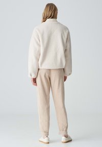Veste en polaire crème avec un col montant et des poignets élastiques, associée à un jogger côtelé beige clair avec des ourlets élastiques et des baskets blanches.