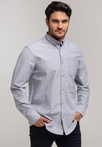 Jasnoniebieska koszula z długim rękawem w fakturowanej tkaninie z naszywaną kieszenią, z klasycznym kołnierzykiem, zestawiona z ciemnymi dżinsami.