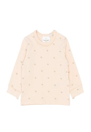 Jasnoróżowa bluzka z długim rękawem z wzorem w złote serca, okrągły dekolt z falbanką oraz zapięciem na zatrzaski na ramieniu.