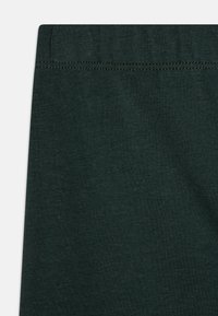 Tissu en coton vert foncé, texture lisse, avec une ceinture élastique cousue. Gros plan sur les détails de la surface du matériau.