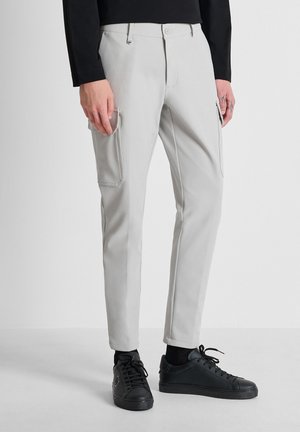 Man draagt lichtgrijze slim-fit cargobroek met zijzakken en zwarte sneakers tegen een effen achtergrond.