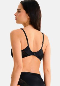 Soutien-gorge noir avec tissu lisse, bretelles ajustables et finition satinée. Vue de dos montrant des détails en dentelle et une fermeture à agrafes.