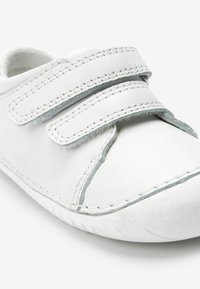 Weiße Schuhe mit zwei Klettverschlüssen. Glattes Leder material mit kontrastierenden Nähten. Abgerundete Spitze und strukturierte Außensohle.