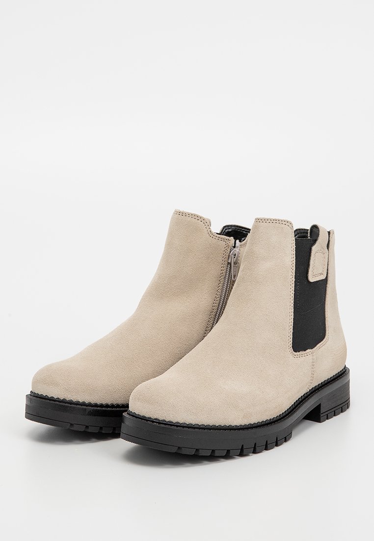 Beige Wildleder-Stiefeletten mit schwarzen elastischen Seitenteilen, einem Reißverschluss und robusten schwarzen Gummisohlen, die eine strukturierte Oberfläche aufweisen.