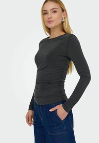 Langærmet tætsiddende top i mørkegrå med rynkede sidedele, rund halsudskæring og glat tekstur, parret med blå denim brede bukser.