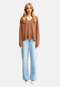 Maglione marrone a maglia con scollo a V, taglia over, abbinato a jeans a gamba larga di colore blu chiaro e tacchi bianchi a punta.