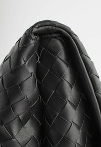 Gros plan sur un matériau en cuir noir tissé plié avec une texture douce et des détails de couture visibles.
