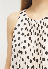 Top senza maniche in tessuto leggero con pois neri, caratterizzato da un design plissettato e scollatura rotonda.