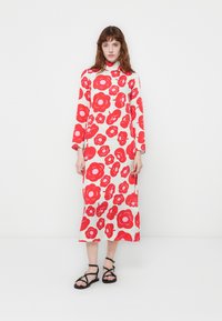 Lang, blomsterkjole med hvid base og store r�øde blomstmønstre, høj hals og lange ærmer. Båret med sorte stroppsandaler.