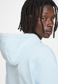 Felpa con cappuccio azzurra chiara dal texture morbida. Presenta una vestibilità comoda e cuciture visibili, progettata con un cappuccio regolabile.