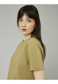 T-shirt à manches courtes vert olive, col rond, en coton doux, coupe légèrement décontractée, détails de couture minimaux.