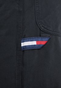 Crna tkanina s ušivenim šavom ima malu tamnoplavu oznaku na kojoj su horizontalne bijele, crvene i plave pruge, što označava identitet branda.