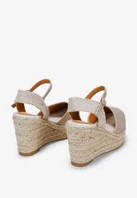 Sandales compensées en tissu beige avec une semelle en jute tissé. Présente une lanière à motif carreauté et un design à bout rond. Lanière arrière pour un maintien sécurisé.