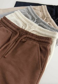 Cotton joggers in brown, beige, grey, light blue, and navy, featuring elastic waistbands with drawstrings and side pockets.