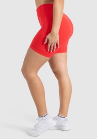 Rode sportieve shorts met een hoge tailleband zijn gemaakt van een gladde, rekbare stof en hebben een getailleerd ontwerp, gecombineerd met witte sneakers.
