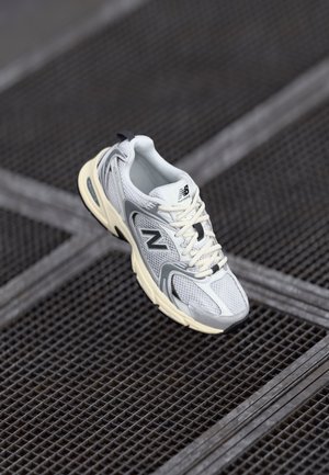 Biało-szary but do biegania New Balance z kremową podeszwą na ciemnej metalowej siatce.