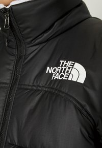 Czarna kurtka ocieplana z widocznym zamkiem błyskawicznym z przodu oraz białym logo The North Face po lewej stronie klatki piersiowej.