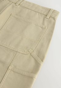 Pantaloni din pânză bej, cu un buzunar posterior, cusături contrastante și un design cu picior drept, având cusături întărite.