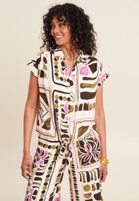 Camicia a maniche corte con bottoni e pantaloni coordinati in crema con audaci motivi geometrici in rosa, verde e nero. Il tessuto sembra leggero.