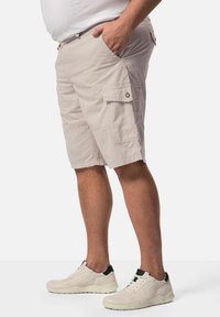Helle beige Cargo-Shorts aus strapazierfähigem Material, mit Seitentaschen und einer lockeren Passform. Kombiniert mit neutralen Sportschuhen.